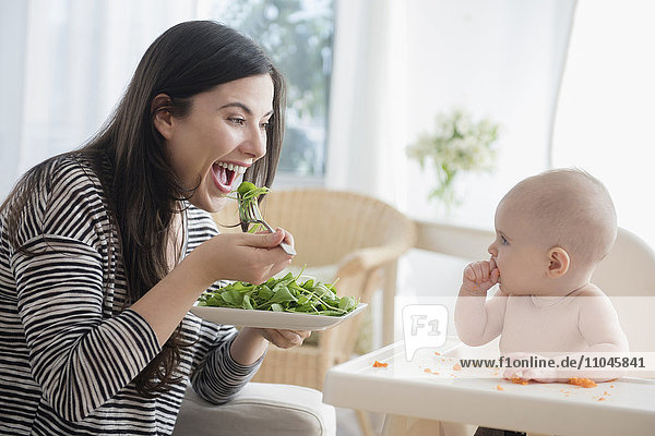 Kaukasische Frau isst Salat und beobachtet ihre kleine Tochter