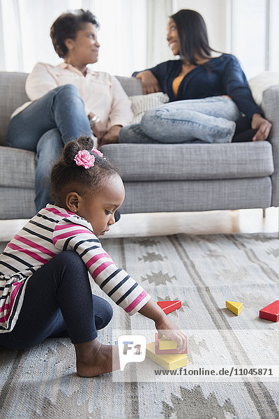 schwarzes Baby Mädchen spielt auf Teppich mit Blöcken