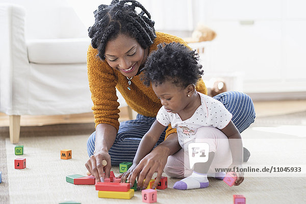 Black mother and baby daughter playing with blocks on carpet