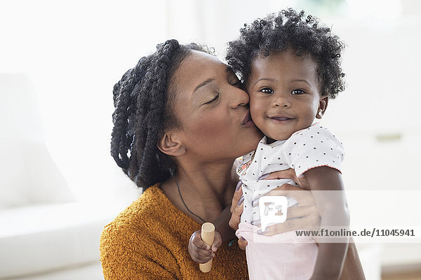 Lächelnde schwarze Mutter küsst ihre kleine Tochter auf die Wange