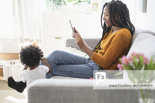 Schwarze Frau benutzt digitales Tablet auf dem Sofa neben ihrer kleinen Tochter