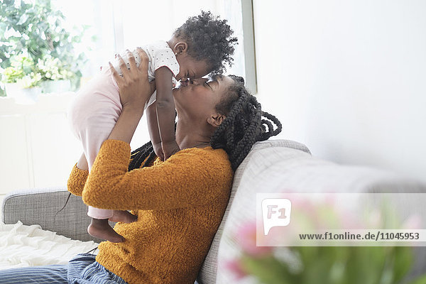Schwarze Frau küsst die Nase ihrer kleinen Tochter auf dem Sofa