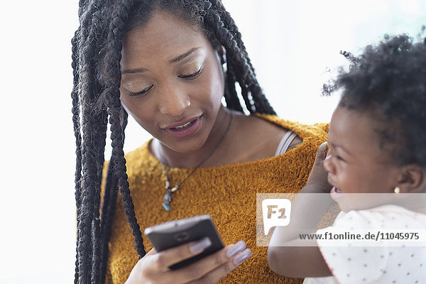Schwarze Frau hält ihre kleine Tochter und benutzt ein Mobiltelefon