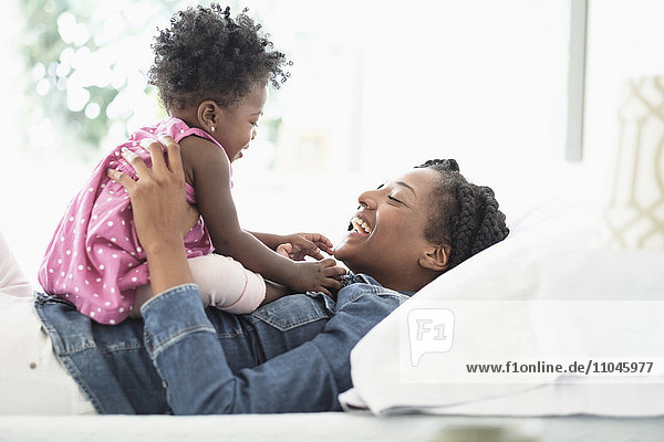 Black woman playing with baby daughter on bed