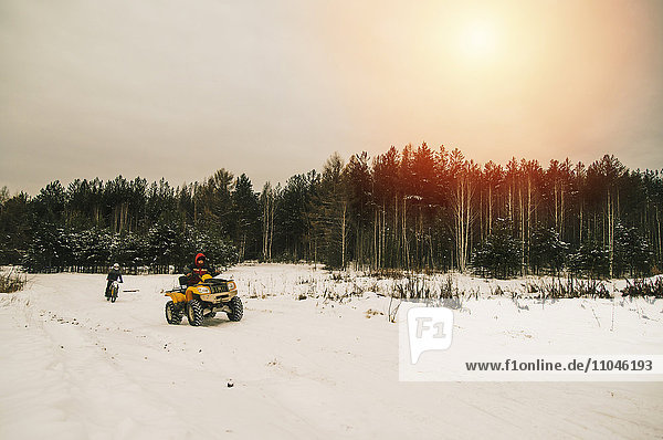 Caucasian men riding all-terrain vehicles in snowy forest