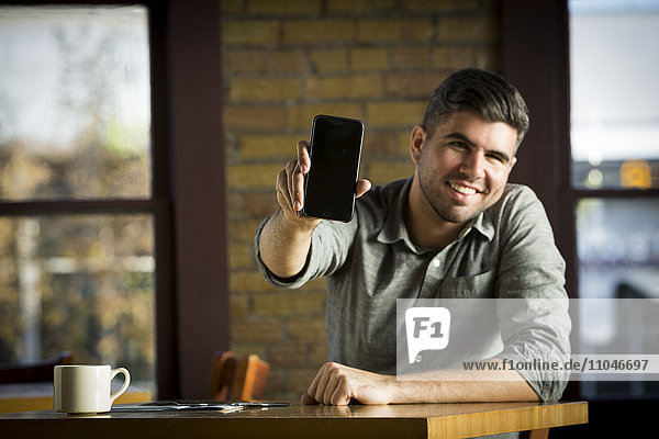 Kaukasischer Mann zeigt Handy im Café