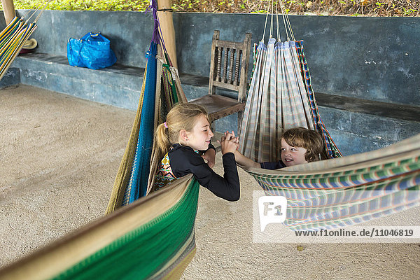 Caucasian brother and sister laying in hammocks holding hands