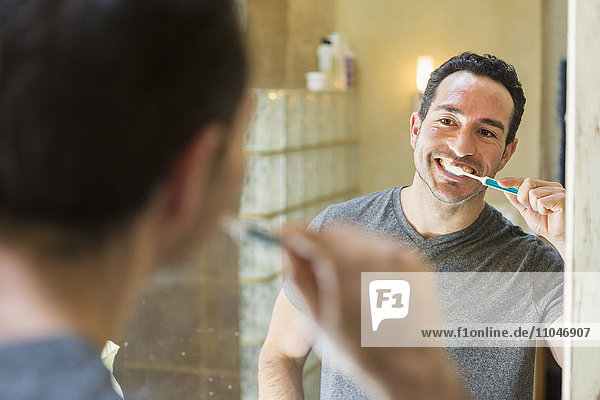 Hispanic man brushing teeth in mirror