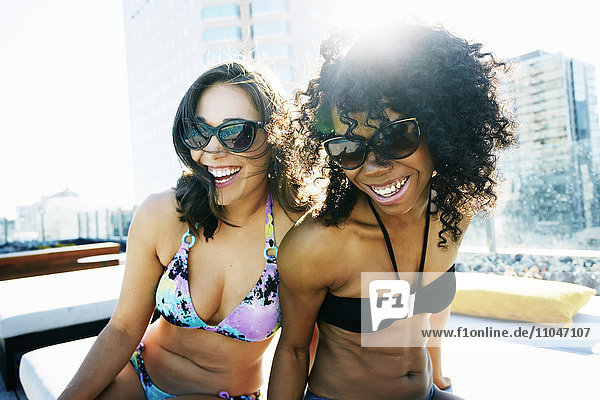 Smiling women wearing bikinis at urban poolside