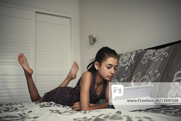 Mixed race girl using digital tablet on bed