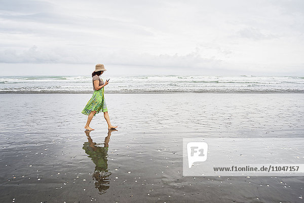 Gemischtrassige Frau geht am Strand mit Handy