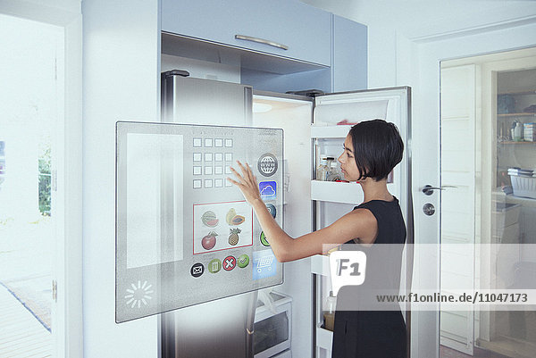 Gemischtrassiges Mädchen mit Hologramm-Kühlschrank-Touchscreen in der Küche