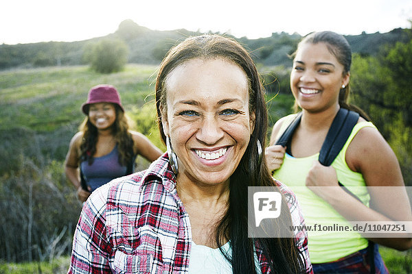 Mixed Race mother and daughters backpacking in field