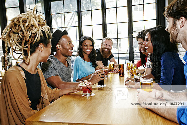 Smiling friends drinking at table in bar