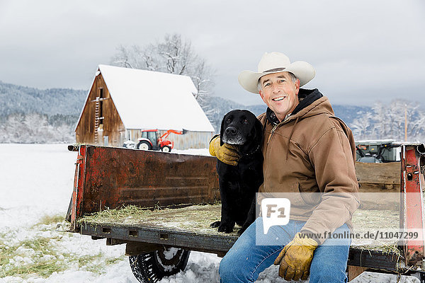 Kaukasischer Bauer umarmt Hund in verschneitem Lastwagen