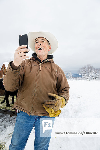 Caucasian farmer using cell phone in snowy field