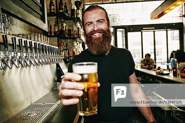 Smiling Caucasian bartender serving beer at bar