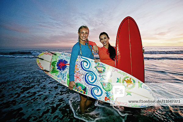 Frauen stehen in den Wellen des Ozeans und halten Surfbretter am Strand
