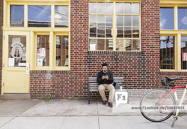 Hispanischer Mann sitzt auf einer Stadtbank und benutzt ein Handy