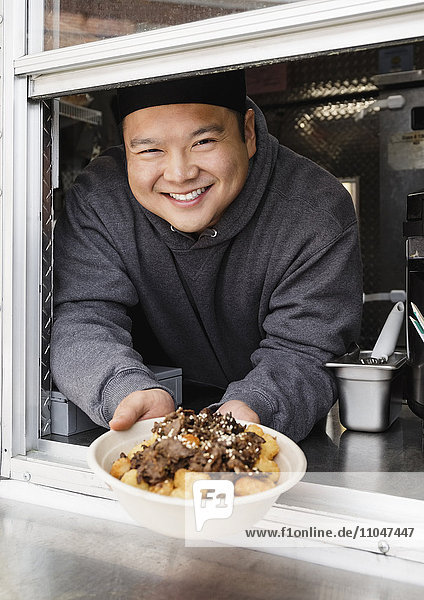 Proud Asian man showing bowl of food at food truck