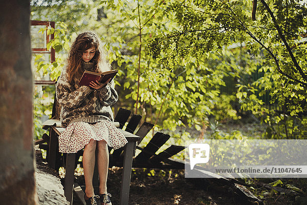 Kaukasisches Mädchen sitzt auf einem Tisch und liest ein Buch