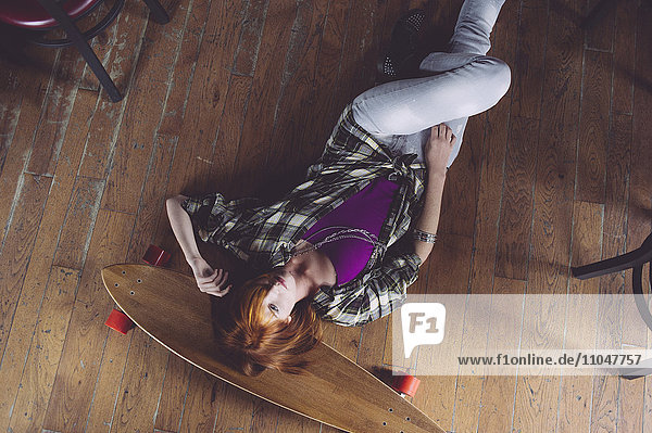 Kaukasische Frau liegt mit Skateboard auf dem Boden