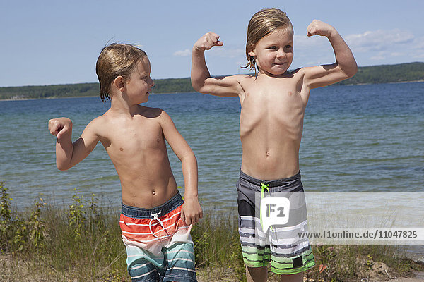 Caucasian boys flexing muscles on beach