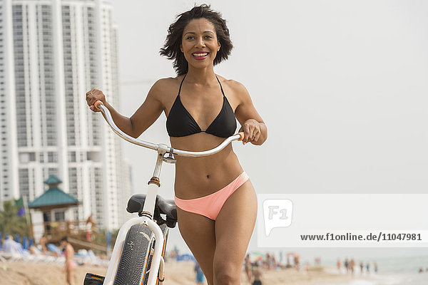 African American woman pushing bicycle on beach