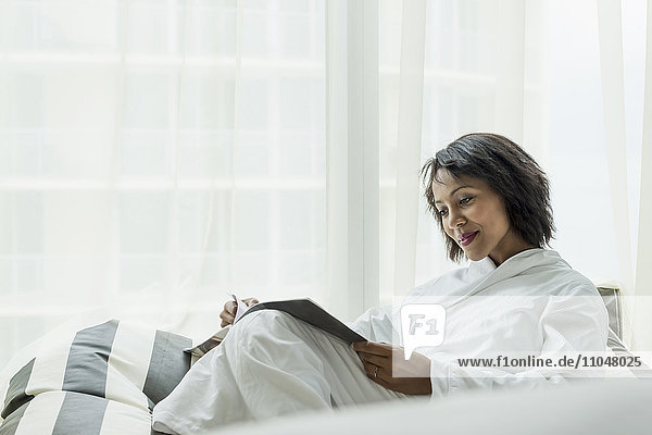 African American woman reading magazine near window