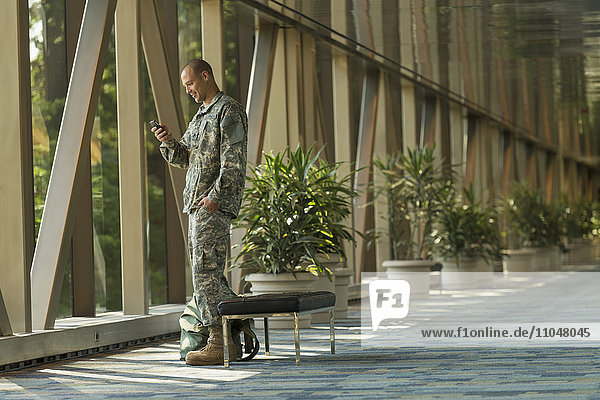 Kaukasischer Soldat benutzt Mobiltelefon im Flughafen