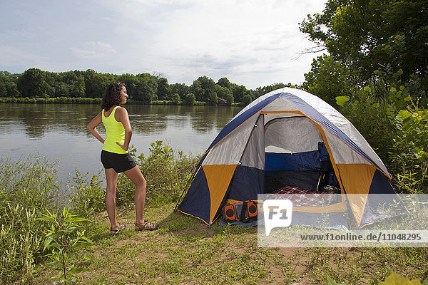 Hispanic woman standing near camping tent at lake
