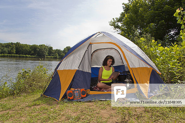 Hispanic woman using digital tablet in camping tent at lake