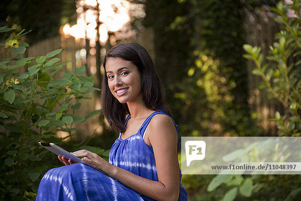 Lächelnde hispanische Frau  die ein digitales Tablet im Hinterhof benutzt
