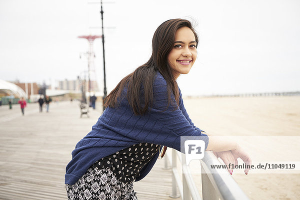 Lächelnde  gemischtrassige Frau  die sich auf das Geländer der Strandpromenade stützt