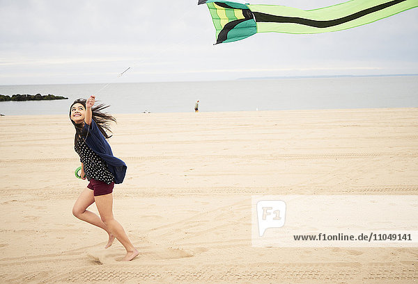 Mixed Race Frau läuft am Strand fliegender Drachen