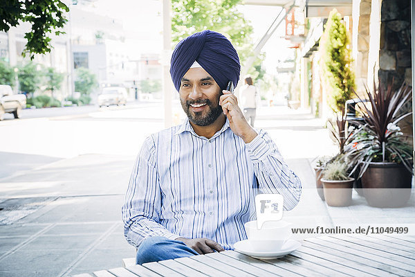 Mann mit Turban  der in einem Café mit einem Handy telefoniert