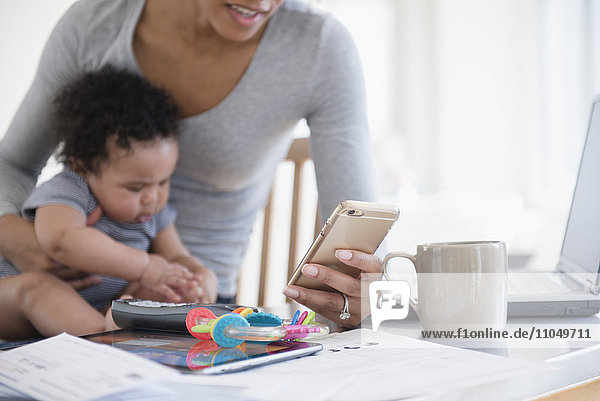 Mother holding baby son in lap texting on cell phone