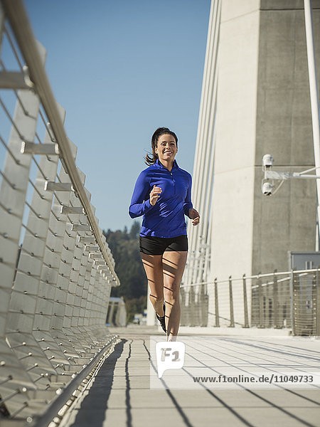Kaukasische Frau joggt auf einer städtischen Brücke