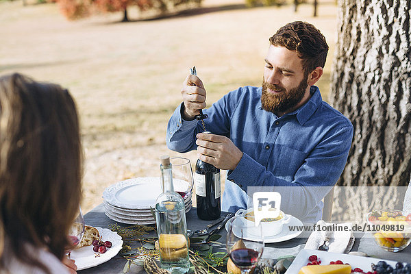 Kaukasischer Mann öffnet Weinflasche an einem Tisch im Freien