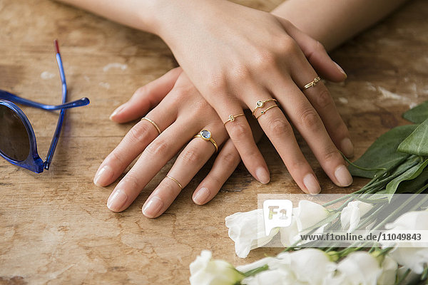 Hände einer hispanischen Frau mit Ringen in der Nähe von Blumen und Sonnenbrille