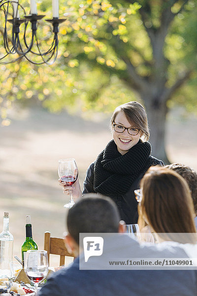 Frau stößt mit Wein an einem Tisch im Freien an