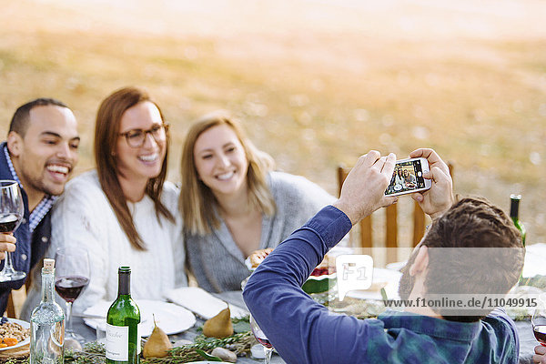 Mann fotografiert Freunde am Tisch im Freien