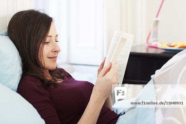 Mixed race woman reading book in bed
