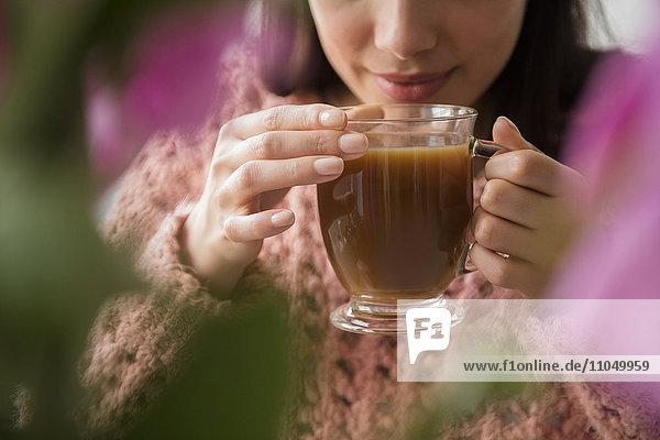 Hispanische Frau trinkt Kaffee hinter Blumen