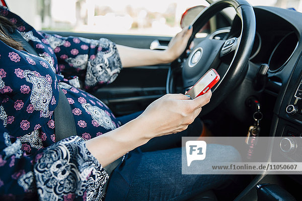 Pregnant Hispanic woman using cell phone and driving