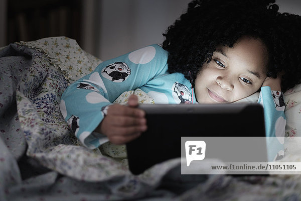 African American girl using digital tablet in bed