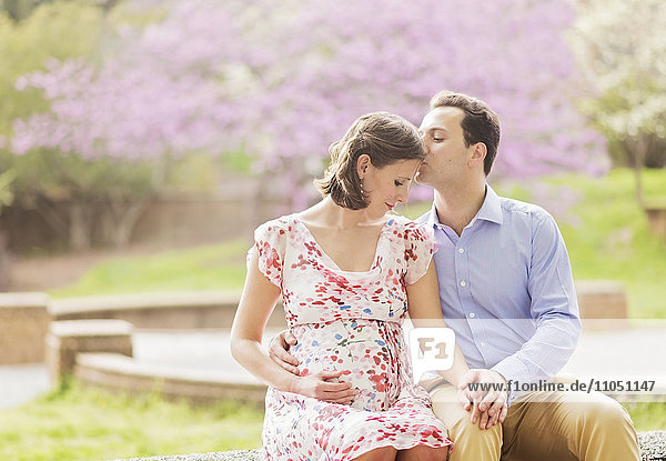 Schwangeres kaukasisches Paar  das sich im Freien küsst