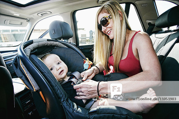 Mother buckling baby son in car seat