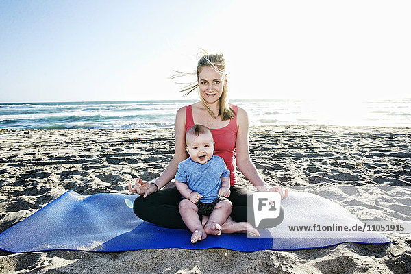 Lächelnde Mutter beim Yoga am Strand mit ihrem kleinen Sohn