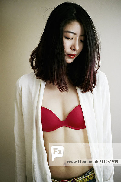 Lächelnde asiatische Frau an der Wand stehend mit rotem BH